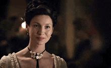 a woman in a white dress and a black necklace is smiling .