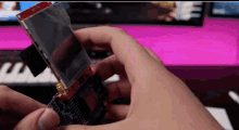 a person is holding a piece of electronic equipment in their hands with a keyboard in the background