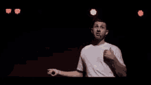 a man in a white shirt is singing into a microphone on a stage in front of red lights .