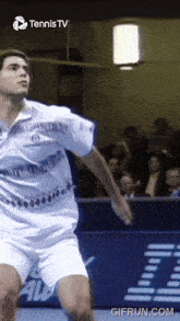 a man in a white shirt and shorts is playing tennis in front of a sign that says tennis tv