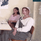 two women are sitting at a table and one is wearing a hat