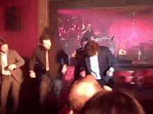 a group of men are dancing on a stage in front of a band