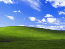 a green hill with a blue sky and white clouds