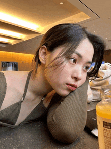 a woman rests her head on her elbow next to a bottle of juice