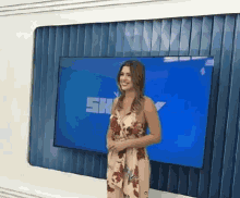a woman in a floral dress is standing in front of a screen that says sh