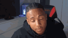 a man in a black hoodie is sitting in a red and black chair with his eyes closed .
