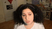 a woman with curly hair wearing headphones with a cuban flag in the background
