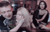 a man is touching a woman 's face while sitting at a table with other people .