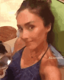 a woman in a blue tank top is taking a selfie with a glass of wine