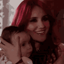 a woman with red hair is holding a baby in her arms and smiling at the camera .
