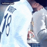 virat kohli is wearing a white shirt with the number 18 on it and holding a trophy .