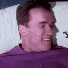 a man in a purple shirt is smiling while laying in bed .