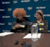 two people wearing texas sweatshirts sit at a table with a bottle of water