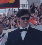 a man in a suit and bow tie is smiling in front of a crowd .