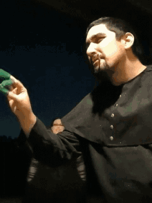 a man in a black robe holds a green object