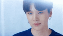 a close up of a young man wearing a blue shirt and earrings looking at the camera .