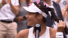 a woman wearing a visor and a hat is talking into a microphone .