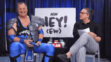 two men are sitting in front of a sign that says hey ew