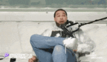 a man is sitting on a couch with his legs crossed in front of a microphone