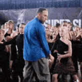 a man in a blue shirt stands in front of a crowd of people dancing