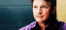 a man in a purple shirt is sitting in front of a blue wall .