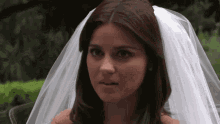 a woman wearing a wedding dress and veil looks at the camera