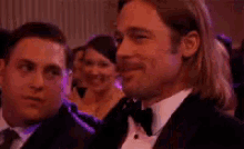 a man in a tuxedo is sitting next to another man in a suit and tie .
