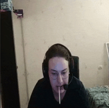 a woman wearing headphones and glasses is smoking a cigarette while sitting in front of a computer .