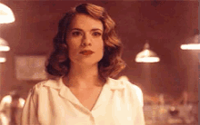 a woman in a white shirt is standing in a room with a blurred background .
