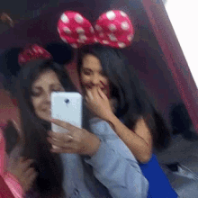 two women wearing minnie mouse ears are taking a picture of themselves