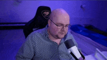 a bald man with glasses is sitting in front of a microphone in a room .