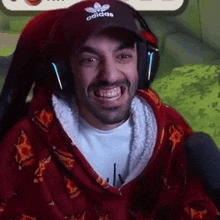 a man wearing headphones and an adidas hat is smiling while sitting in a chair .