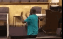 a man in a blue shirt is standing in a church holding a chair .