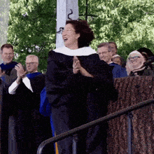 a woman in a graduation cap and gown stands in front of a crowd