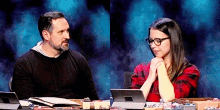 a man and a woman are sitting at a table with their hands folded in prayer .