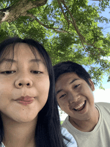 a man and a woman are posing for a picture under a tree and smiling