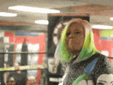 a woman with green hair and pink hair is standing in a boxing ring .