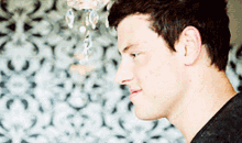 a close up of a man 's face with a chandelier hanging in the background