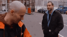 two men are standing next to each other in a parking lot talking to each other .