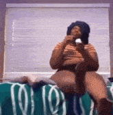 a woman is sitting on a bed eating an ice cream cone while talking on a cell phone .