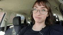 a woman wearing glasses and a black shirt is sitting in the back seat of a car