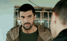 a man with a beard wearing a green sweater and a brown jacket