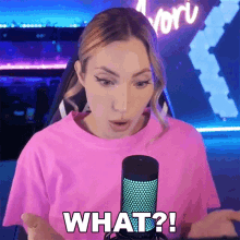 a woman in a pink shirt is talking into a microphone and says what