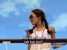 a woman wearing sunglasses and a braided hair says ada ikan besar tak kat sini in a foreign language