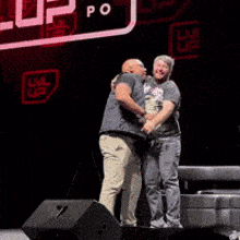 two men are hugging on a stage in front of a sign that says " up "