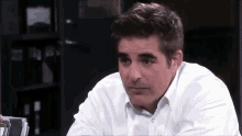 a man in a white shirt is sitting at a desk looking at something .