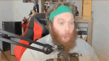 a man with a beard is sitting in front of a microphone wearing a green headband .