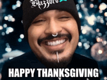 a man with a beard wearing a black beanie and a piercing in his nose is smiling and says happy thanksgiving