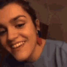 a woman wearing a blue shirt and red earrings is smiling and looking at the camera .
