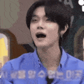 a young man in a blue shirt is making a funny face with his mouth wide open .